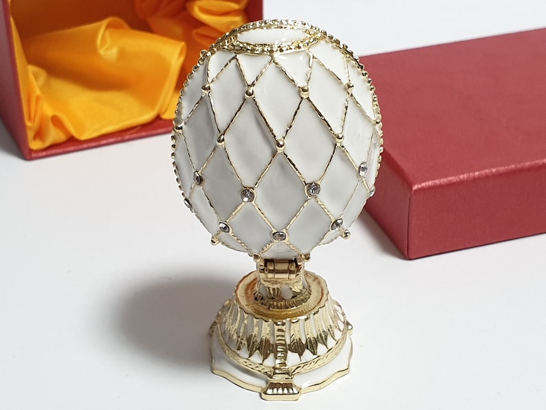 May include: A white porcelain egg with a gold lattice design and clear rhinestones. The egg is on a gold stand with a decorative base.