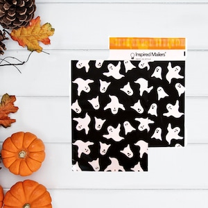May include: Black and white ghost-patterned mailer bags. The bags are decorated with white cartoon ghosts on a black background. The bags are next to a package with the text "Inspired Mailers" and pumpkins and fall foliage.