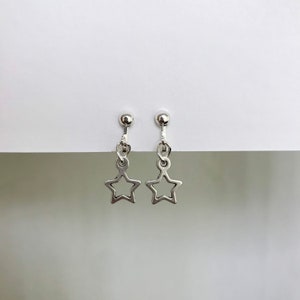 May include: A pair of silver clip-on earrings with a star charm dangling from each. The stars are hollow and have a simple design.