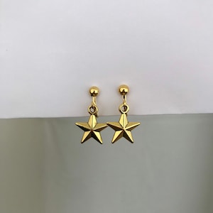 Könnte beinhalten: Ein Paar goldene Ohrringe mit Sternform und Clipverschluss.