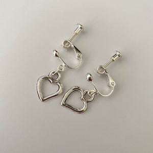 May include: A pair of silver clip-on earrings with heart-shaped charms. The earrings have a screw-on closure.