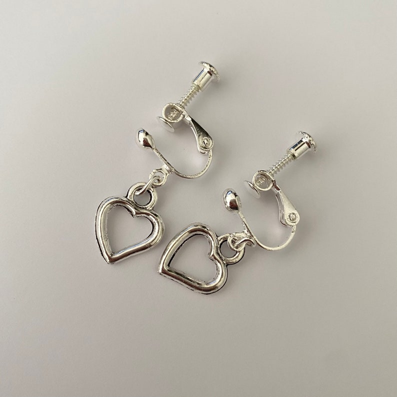 May include: A pair of silver clip-on earrings with heart-shaped charms. The earrings have a screw-on closure.