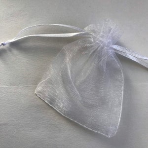 May include: A white organza gift bag with a drawstring closure. The bag is made of sheer fabric and is perfect for small gifts or favors.