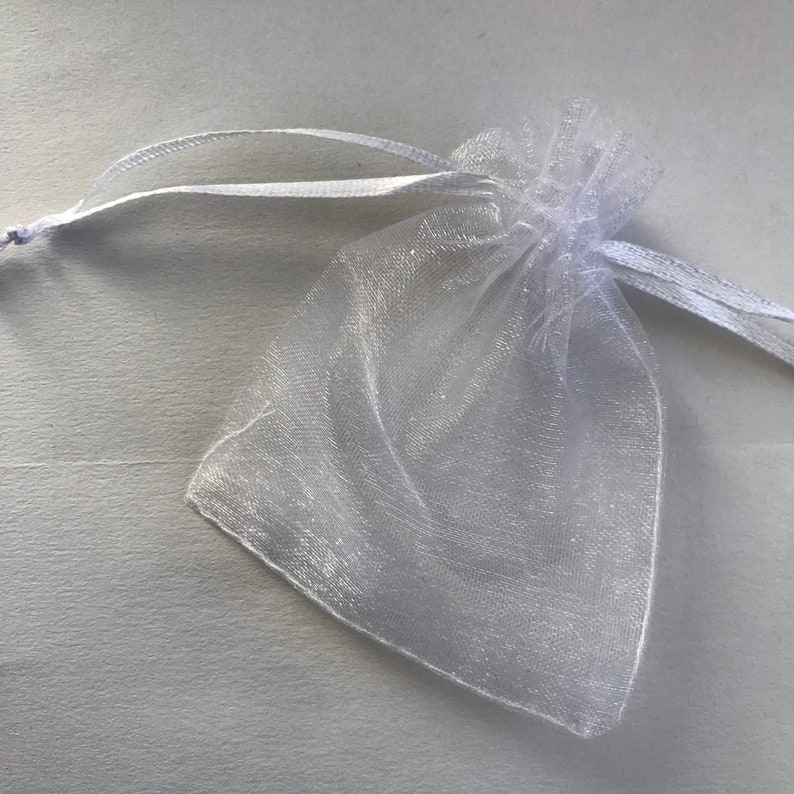 May include: A white organza gift bag with a drawstring closure. The bag is made of sheer fabric and is perfect for small gifts or favors.