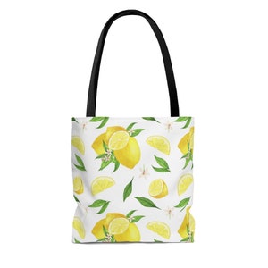 May include: A white tote bag with black handles features a repeating pattern of yellow lemons, green leaves, and white flowers.