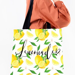 May include: A white tote bag with black handles and a lemon print. The bag has the word "Lemonade" written in black cursive lettering.