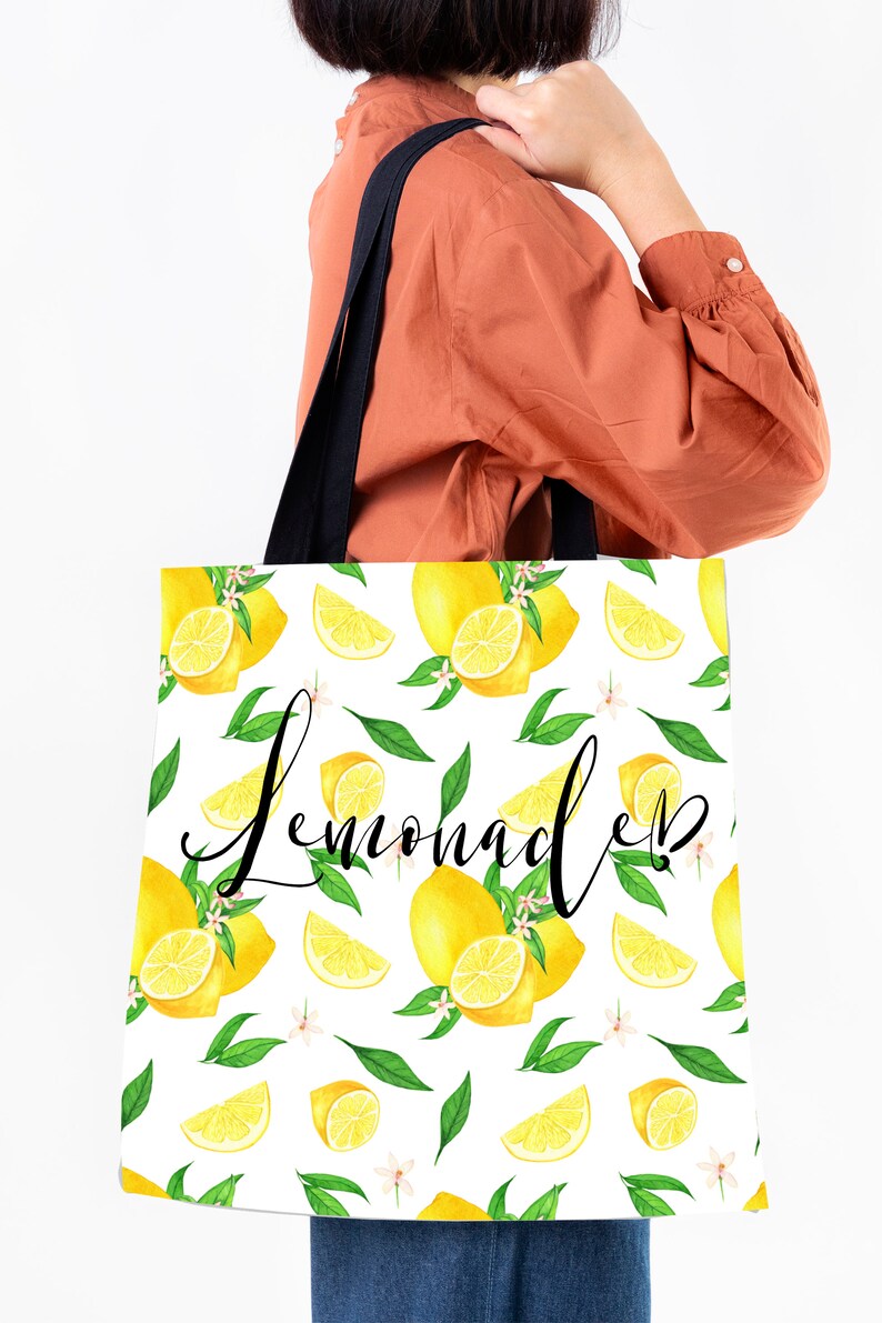 May include: A white tote bag with black handles and a lemon print. The bag has the word "Lemonade" written in black cursive lettering.