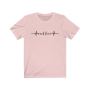 May include: A pink t-shirt with a black graphic of a heartbeat with the word "coffee" inside.