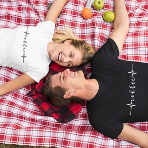 May include: A couple wearing matching t-shirts with a heartbeat graphic and the text "woo-hoo-eep" on a red and white checkered blanket.