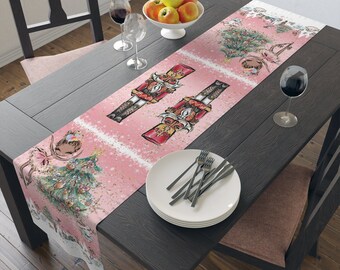 May include: Pink Christmas table runner with a Nutcracker and ballerina design. The runner features a pink background with white snowflakes and a green Christmas tree.