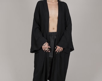 Peut inclure: Un kimono noir à manches longues avec un devant large et ouvert. Le kimono est porté sur un pantalon noir et des bottes noires.