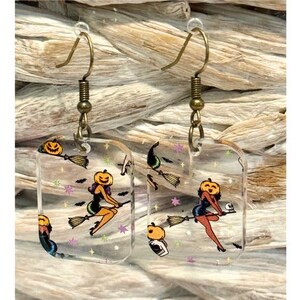 Rechthoekige halloween lichtgewicht acryl hangoorbellen met een heks met pompoenkop op een bezem.