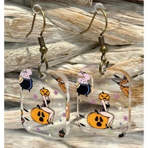 Lichtgewicht rechthoekige Halloween-oorbellen van helder acryl met een dame zittend op een pompoen en een heksenketel.