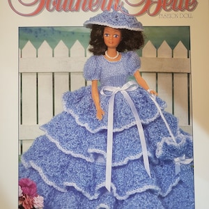May include: A knitting pattern cover featuring a fashion doll in a blue knitted dress, hat, and purse. The doll has dark hair and a pearl necklace. The text reads "Southern Belle Fashion Doll" and "Knit This Beautiful Fashion Doll Outfit!"