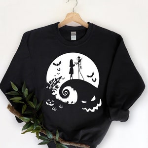 May include: Black sweatshirt with a white graphic of Jack Skellington and Sally from The Nightmare Before Christmas standing on a hill with a full moon and bats in the background. The hill is shaped like a jack-o-lantern with a spooky house and pumpkins in the foreground.