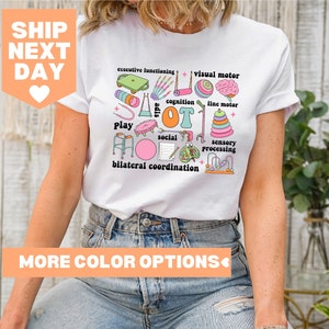Pode incluir: Camiseta branca com um design gráfico colorido que apresenta a palavra "OT" cercada por várias ferramentas de terapia ocupacional e as palavras "funcionamento executivo", "motricidade visual", "cognição", "motricidade fina", "brincar", "social", "processamento sensorial" e "coordenação bilateral".