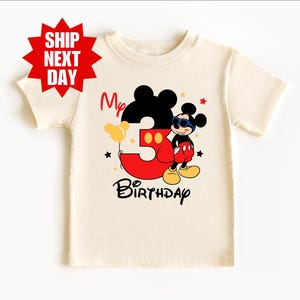 May include: A white t-shirt with a Mickey Mouse design. The design features Mickey Mouse holding a balloon with the number 3 and the text "My 3rd Birthday".