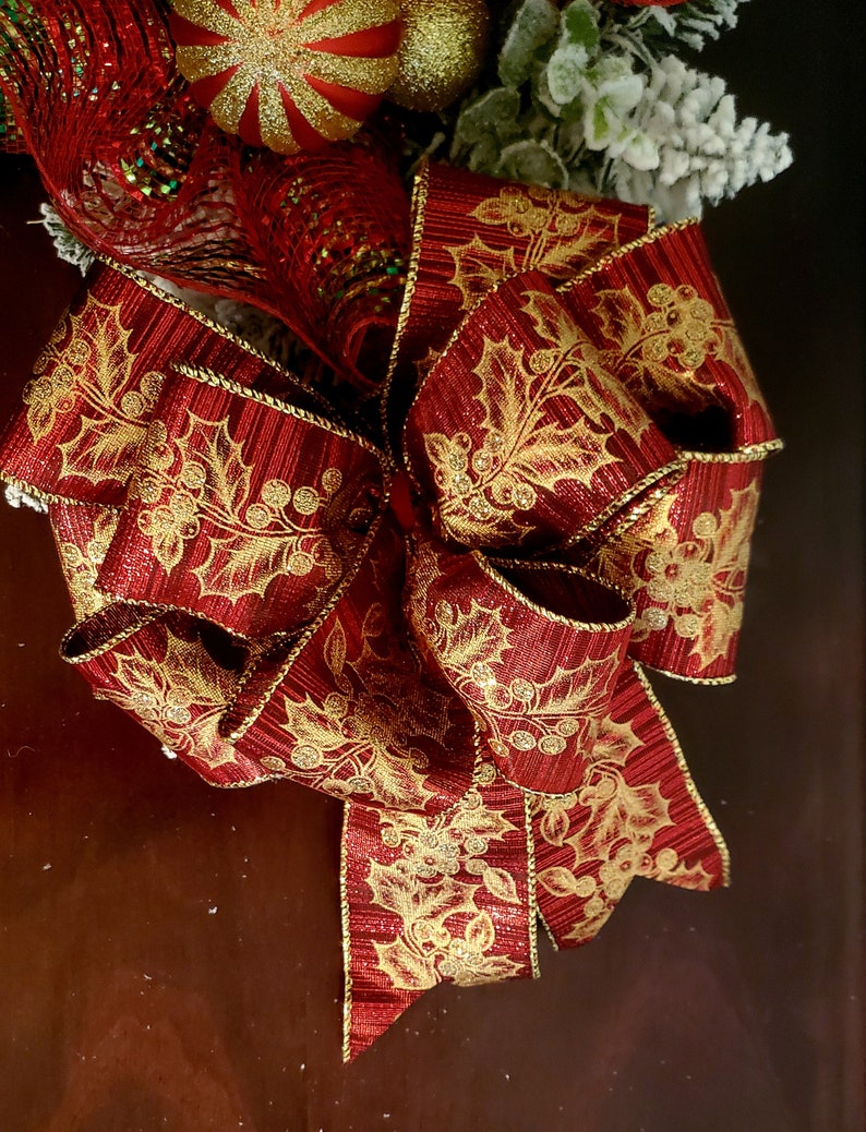 May include: A red and gold Christmas bow with a holly leaf pattern. The bow is made of a shiny, textured fabric.