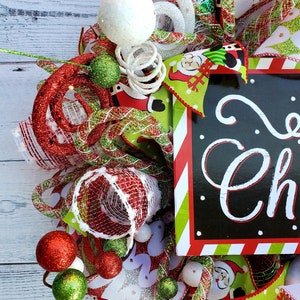 May include: A festive Christmas wreath with red, green, and white accents. The wreath features decorative balls, ribbons, and a sign that says "Merry Christmas". The design includes Santa Claus imagery and glittery embellishments.