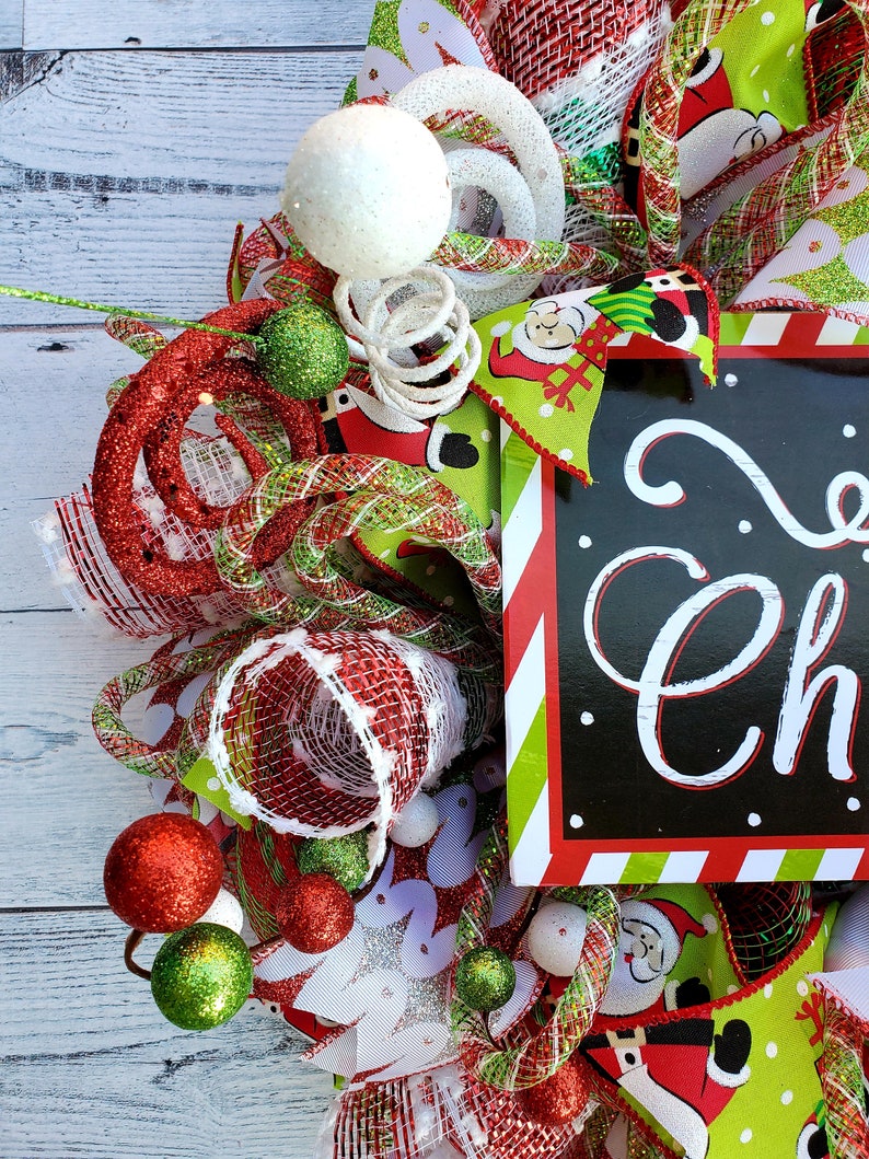 May include: A festive Christmas wreath with red, green, and white accents. The wreath features decorative balls, ribbons, and a sign that says "Merry Christmas". The design includes Santa Claus imagery and glittery embellishments.