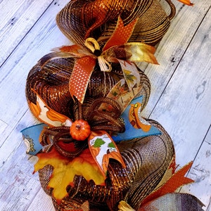 May include: A brown and gold mesh pumpkin garland with orange and brown ribbon accents. The garland features a fall leaf and a small orange pumpkin.