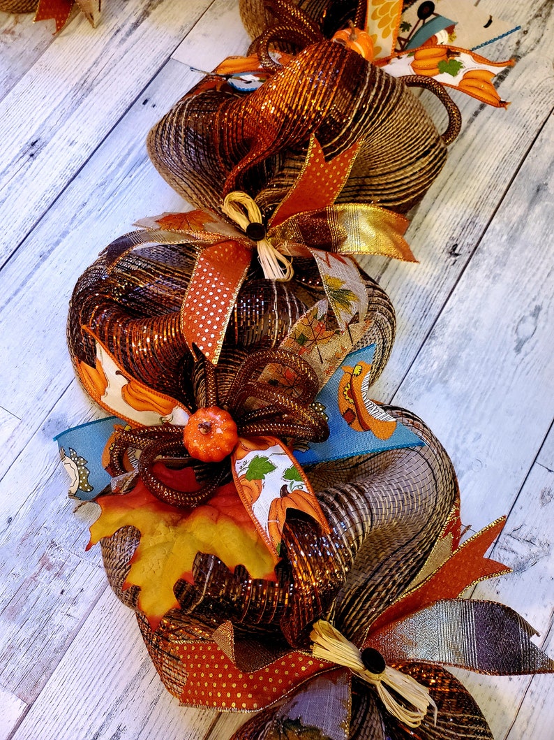 May include: A brown and gold mesh pumpkin garland with orange and brown ribbon accents. The garland features a fall leaf and a small orange pumpkin.