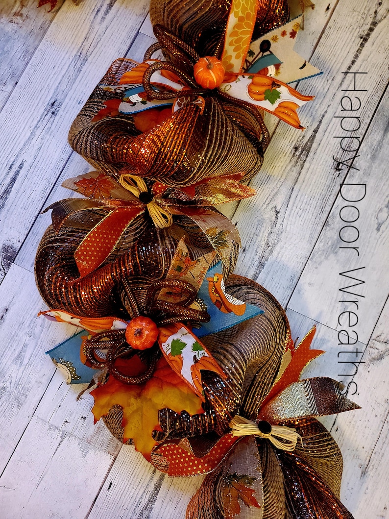 May include: A brown, orange, and gold fall wreath with a burlap bow and small pumpkins. The wreath is made of mesh and has a variety of fall-themed decorations. The text "Happy Door Wreaths" is visible in the background.