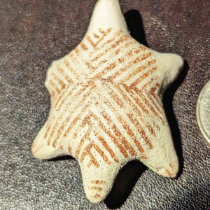 May include: A white ceramic star with a brown geometric pattern. The star is a 3D object with a raised surface.