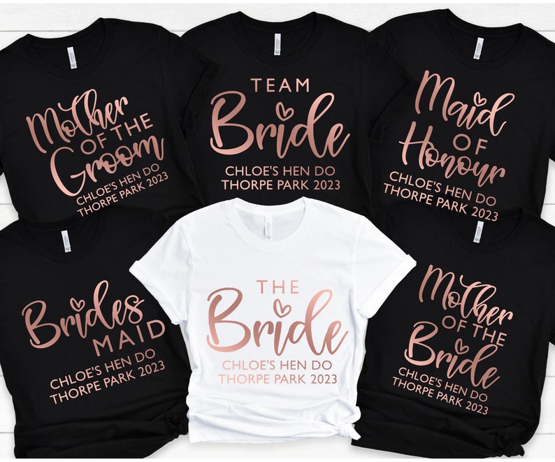 May include: Six black and white t-shirts with rose gold text. The shirts say "Mother of the Groom", "Team Bride", "Maid of Honour", "Brides Maid", "The Bride", and "Mother of the Bride". Each shirt also includes the text "Chloe's Hen Do Thorpe Park 2023".