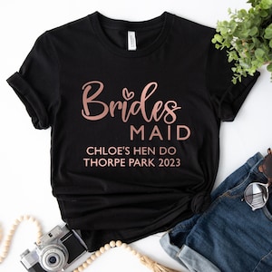 May include: Black t-shirt with rose gold text that reads "Brides Maid Chloe's Hen Do Thorpe Park 2023".