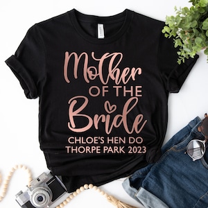 May include: Black t-shirt with rose gold text that reads "Mother of the Bride" with a small heart. Below the text is "Chloe's Hen Do Thorpe Park 2023".