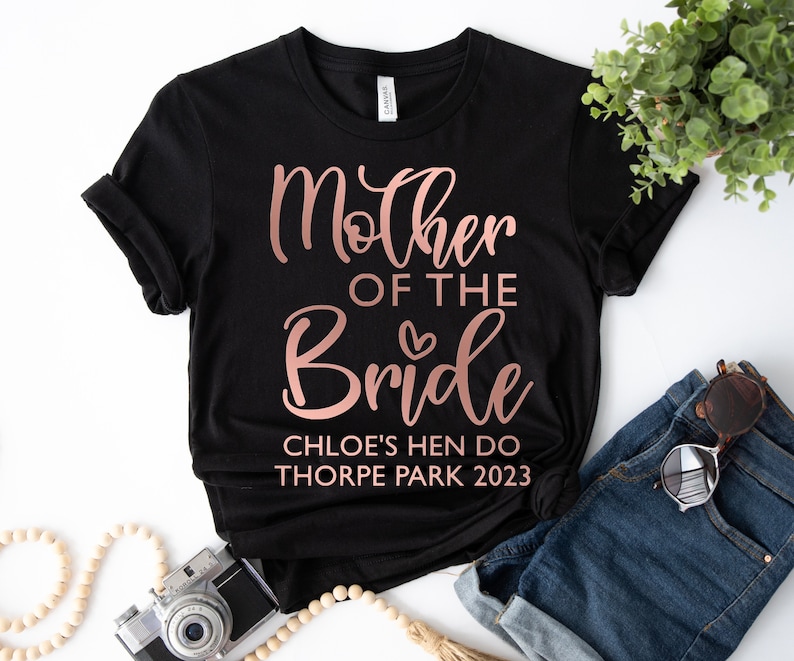 May include: Black t-shirt with rose gold text that reads "Mother of the Bride" with a small heart. Below the text is "Chloe's Hen Do Thorpe Park 2023".
