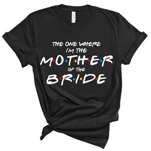 May include: Black t-shirt with white text that reads "The One Where I'm The Mother Of The Bride" with colorful dots around the letters.