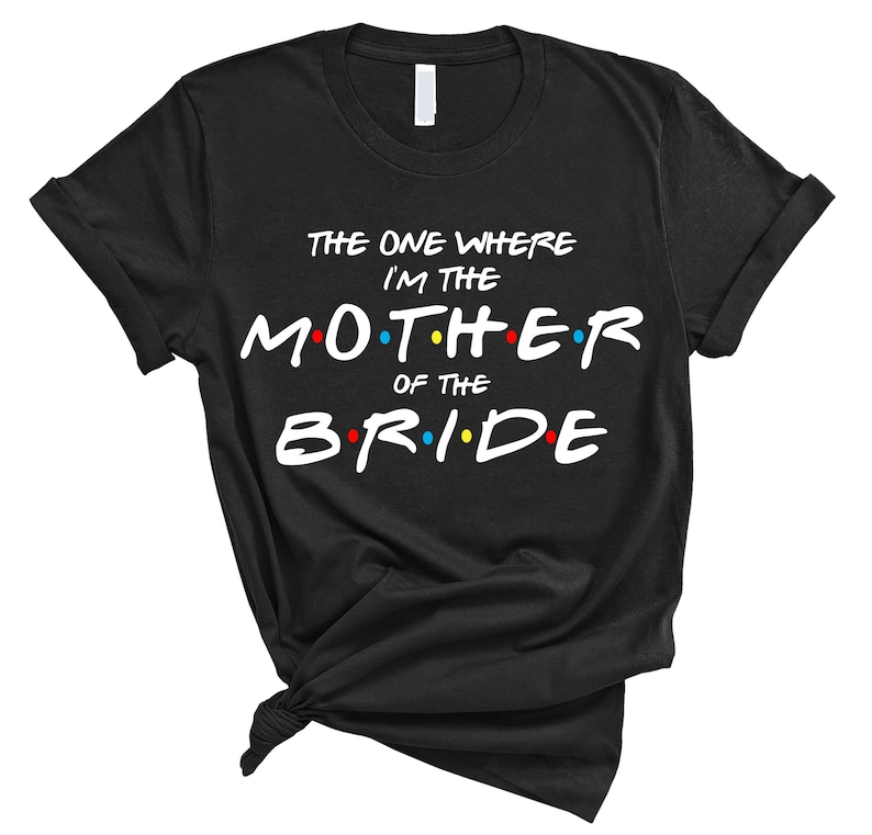 May include: Black t-shirt with white text that reads "The One Where I'm The Mother Of The Bride" with colorful dots around the letters.