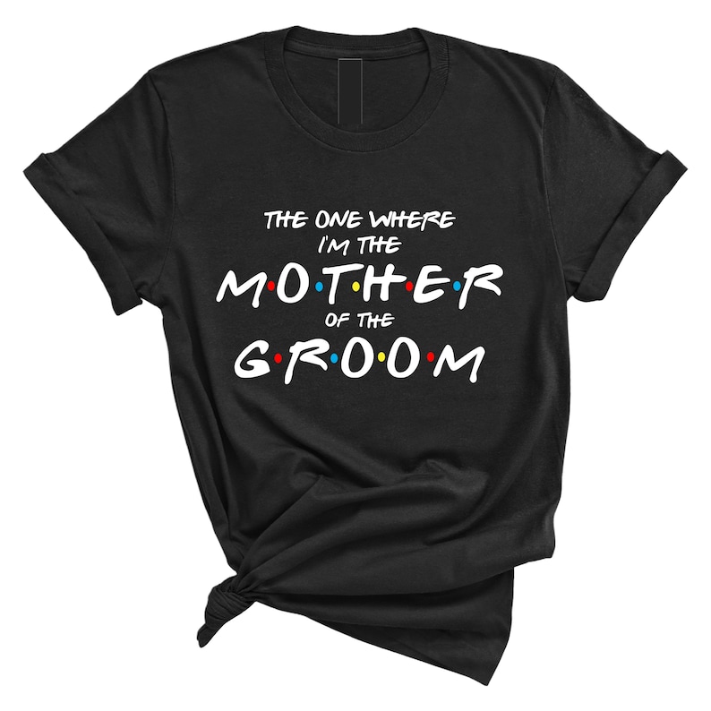 May include: Black t-shirt with white text that reads "The One Where I'm The Mother Of The Groom" in a font reminiscent of the popular TV show "Friends".