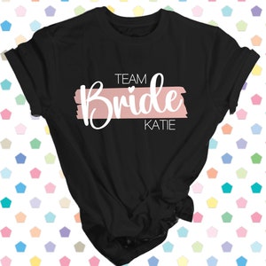 May include: Black t-shirt with a pink stripe and the text "Team Bride Katie" in white.