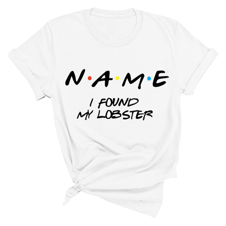 May include: White t-shirt with black text that reads "N.A.M.E. I FOUND MY LOBSTER". The letters in "NAME" are in a stylized font and have colored dots between them.