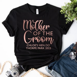 May include: Black t-shirt with rose gold text that reads "Mother of the Groom" and "Chloe's Hen Do Thorpe Park 2023".