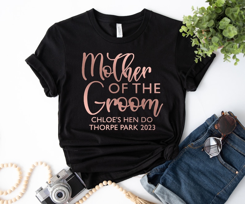 May include: Black t-shirt with rose gold text that reads "Mother of the Groom" and "Chloe's Hen Do Thorpe Park 2023".