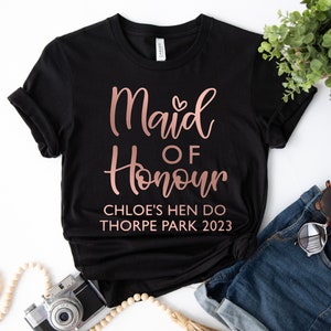 May include: Black t-shirt with rose gold text that reads "Maid of Honour Chloe's Hen Do Thorpe Park 2023".