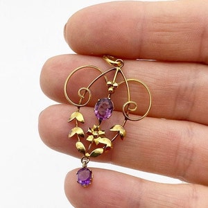 May include: A gold pendant with a delicate floral design and amethyst gemstones. The pendant features a central amethyst stone surrounded by smaller amethyst stones and gold leaves.