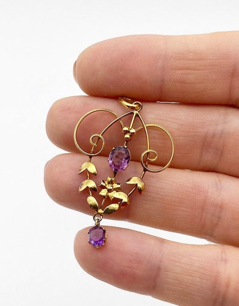 May include: A gold pendant with a delicate floral design and amethyst gemstones. The pendant features a central amethyst stone surrounded by smaller amethyst stones and gold leaves.