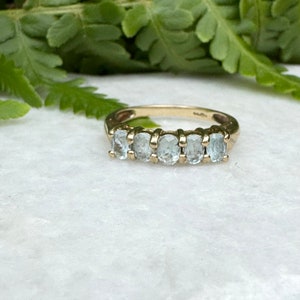May include: A gold band ring with six oval-shaped aquamarine gemstones set in a row.