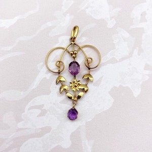 May include: A gold pendant with a delicate floral design and three amethyst stones. The pendant is made of gold and features a floral motif with leaves and a flower. The amethyst stones are oval-shaped and are set in the center of the pendant.