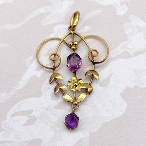 May include: A gold pendant with a delicate floral design and two amethyst stones. The pendant features a central flower with leaves and two oval-shaped amethysts.