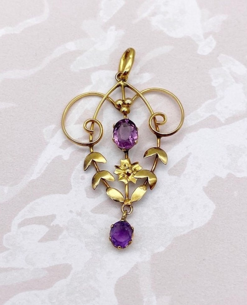 May include: A gold pendant with a delicate floral design and two amethyst stones. The pendant features a central flower with leaves and two oval-shaped amethysts.
