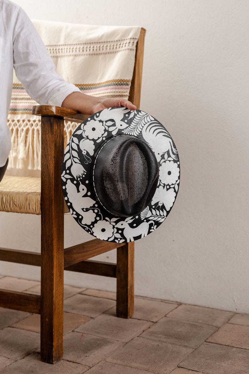 May include: A black and white straw hat with a floral and animal design. The hat has a black mesh crown and a wide brim.
