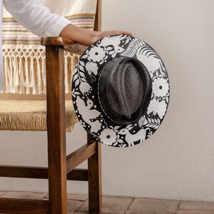 May include: A black and white hat with a floral design. The hat has a wide brim and a black band around the crown.