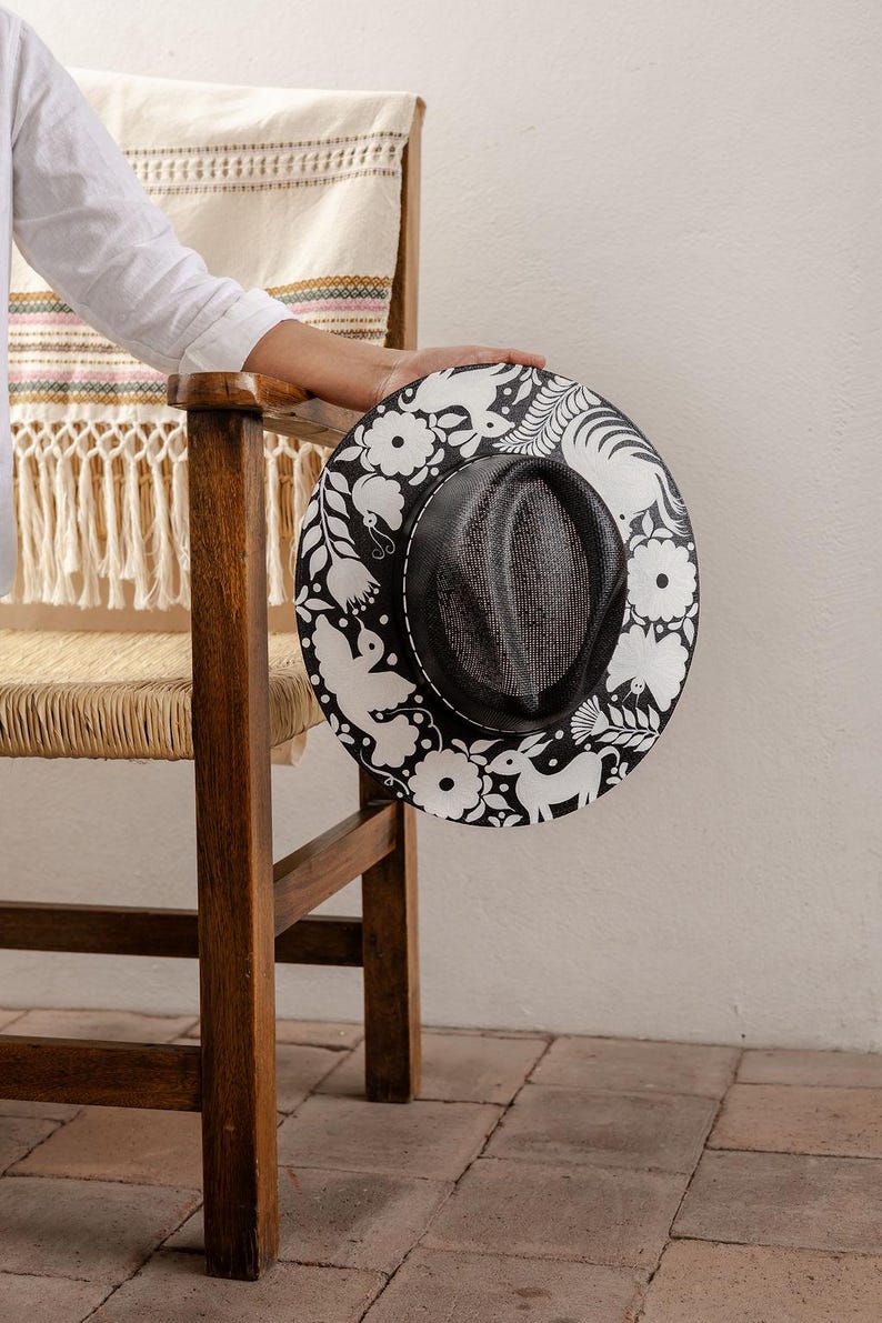 May include: A black and white hat with a floral design. The hat has a wide brim and a black band around the crown.