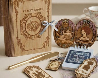 May include: A collection of wooden items with a vintage theme. Includes a book-shaped box with "Society Papers" text, decorative oval plaques, a gold letter opener, a small notepad, and keychains. The items are light brown with engraved designs.